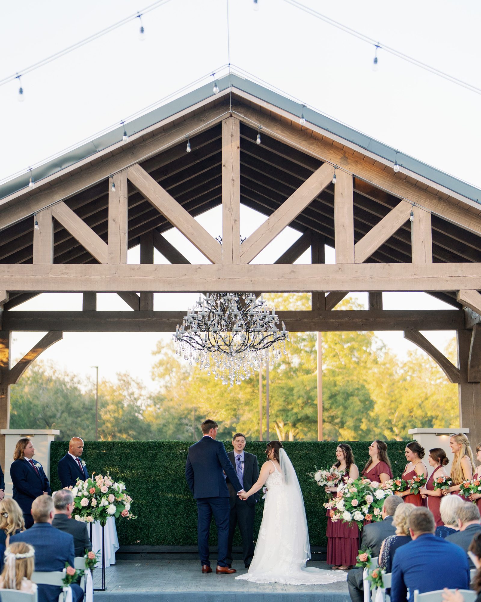 Wedding ceremony under the timber-frame pavilion at The Stables on the Brazos, with a chandelier above the couple