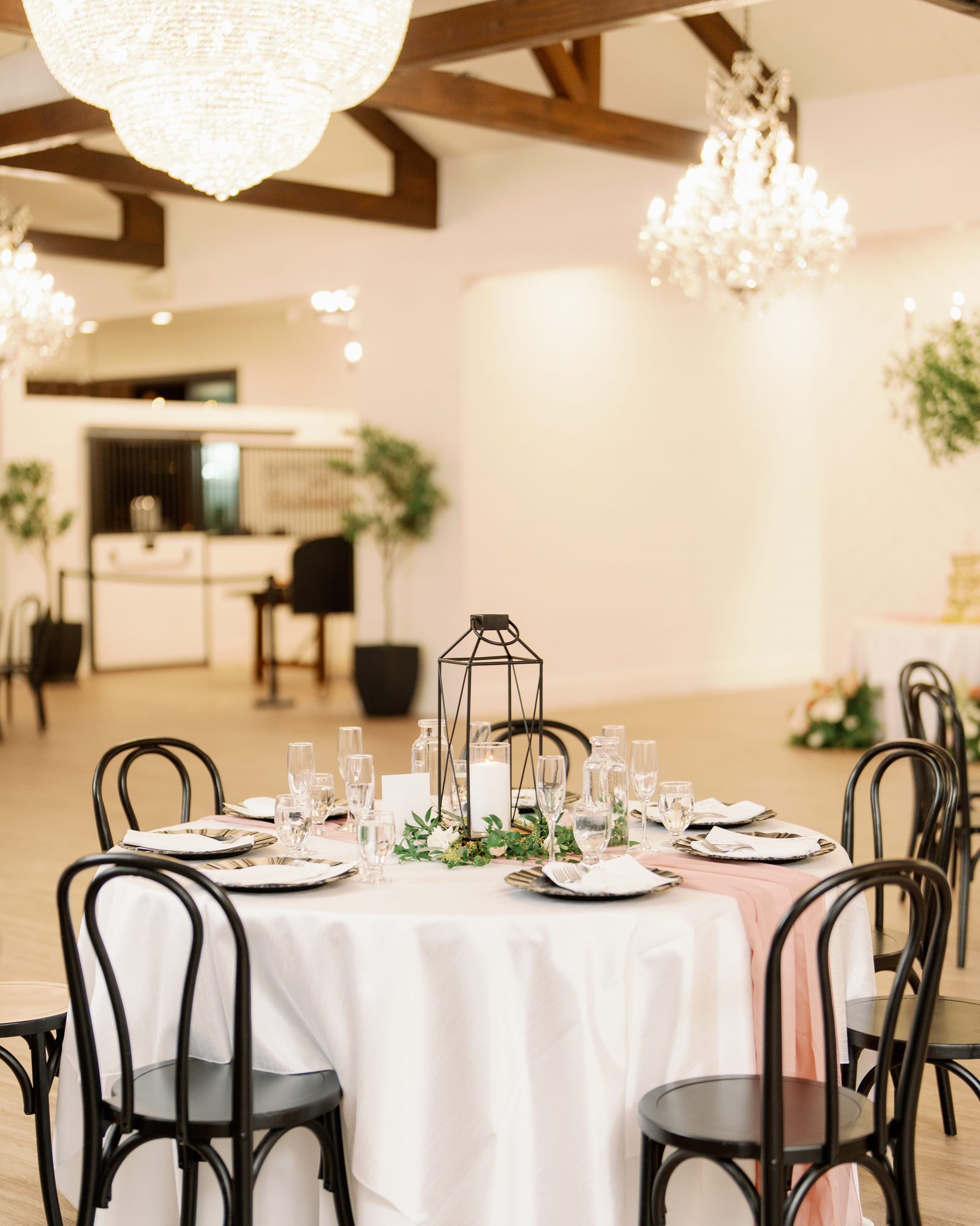The Stables on the Brazos ballroom set for a reception — chandeliers, wood beams, and black bentwood chairs around white-linen tables